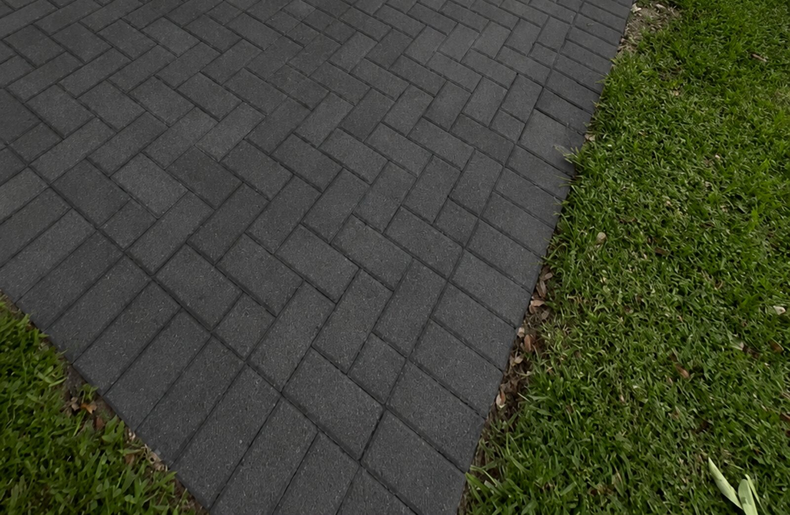 Herringbone pavers stained a deep charcoal black beside a lawn